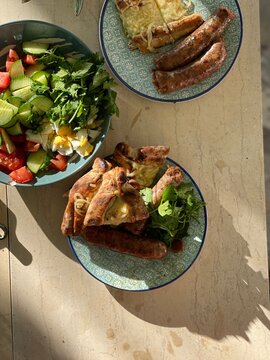 An appetizing composition of grilled sausages, fresh salad with eggs, and cheese-filled p