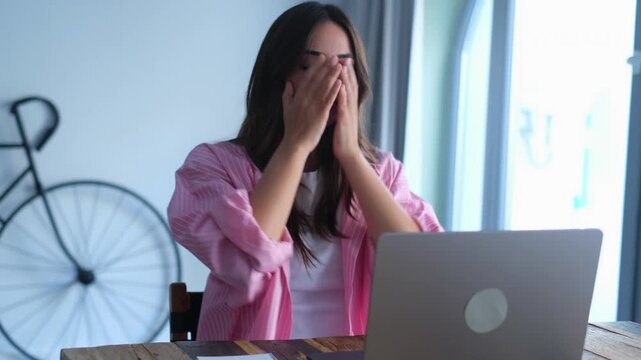 A young woman working on her laptop becomes visibly frustrated and stressed, demonstrating her struggle with a challenging task. She eventually regains composure and continues her focused work.