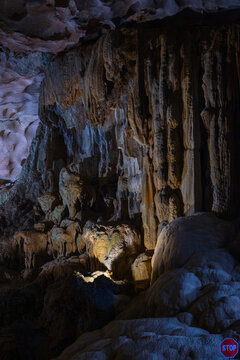 Colorful illuminated limestone cave interior in Vietnam with massive stalactites and stalagmites textured rock walls dramatic shadows and underground geological formations natural travel destination 