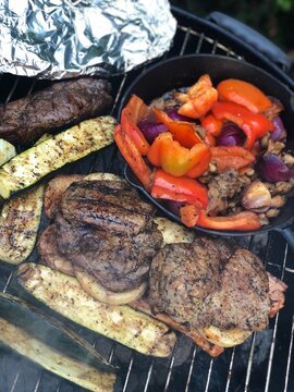 Close-up of a charcoal grill with grilled steak and various vegetables like peppers, onio