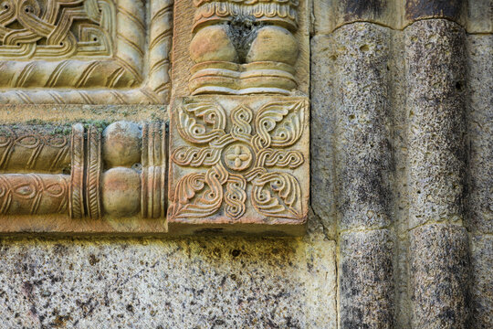 Weathered stone relief at gergeti trinity church in kazbegi showing a symmetrical quatrefoil with swirling scrolls and interwoven bands, a medieval ornamental motif
