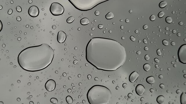 Raindrops dripping onto panoramic glass from above, close-up