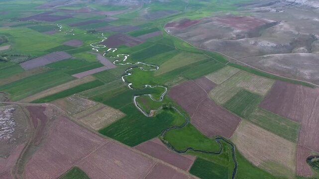 Aerial view of river meander flowing through agricultural fields on a flat plain in France. Spring season, rural plains, and watercourse support rural farming themes and seasonal production.
