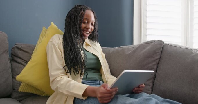 Teenage Girl Using Digital tablet doing Homework on Sofa in Living room