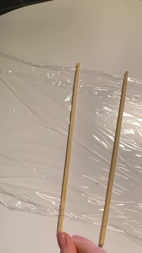 Vertical top view video: plastic wrap is spread on a white table, wooden sticks are placed on it with spacing