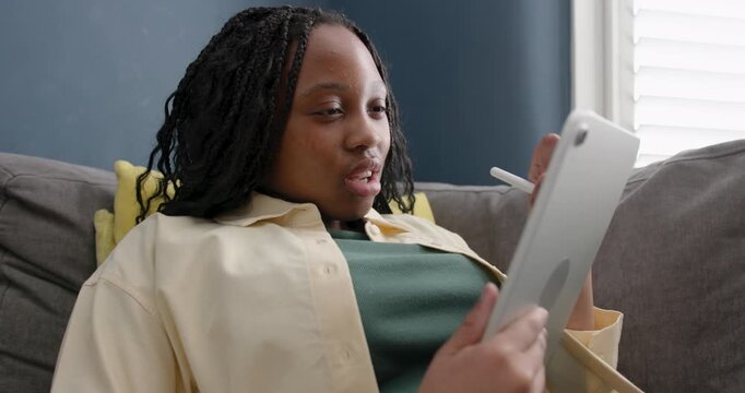 Teenage Girl Using Digital tablet doing Homework on Sofa in Living room