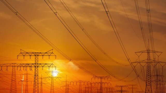 sunset time-lapse over a industrial landscape with high voltage transmissions towers, wind turbine and power lines grid for energy, symbolic concept with copy space, beautiful evening sunlight