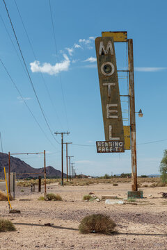 A weathered and deteriorating vintage roadside motel sign stands in an arid desert landscape under a blue sky with scattered white clouds.