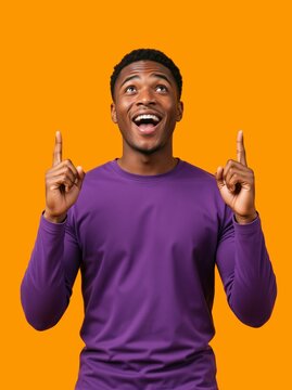 Vertical portrait of an excited young Black man pointing up. Happy African American male in a purple shirt looking upwards in surprise against an orange background. Copy space for text