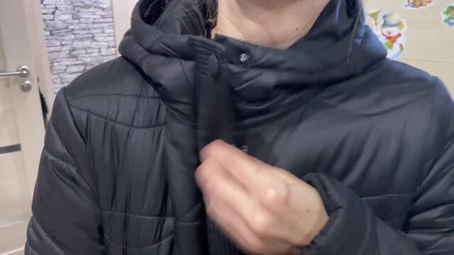 Individual dons jacket. Person adjusting outerwear inside home. Someone prepares for day by adjusting clothing. Individual secures their jacket hood and zipper before heading out in morning