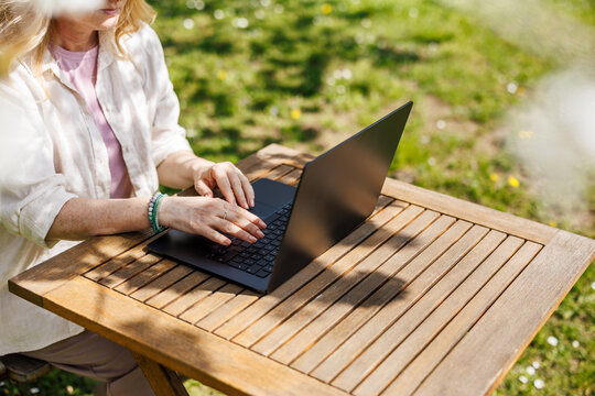 Freelancer working on laptop in garden. Woman using computer at outdoor desk in backyard. Remote work from home in sunny day