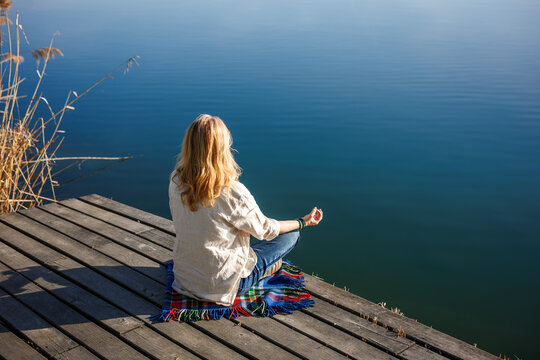 Meditation in lotus pose on wooden jetty. Woman practicing yoga on dock by lake finding inner peace in quiet nature