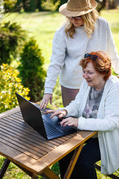 Senior mother learning digital skills and modern technology from her adult daughter. Elderly woman using laptop outdoors