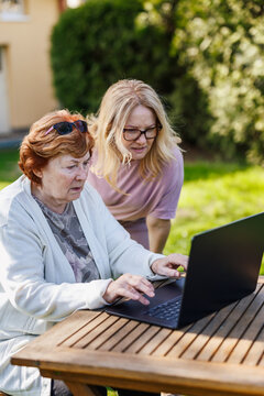 Elderly woman using laptop outdoors. Senior mother learning modern technology and digital skills from her adult daughter