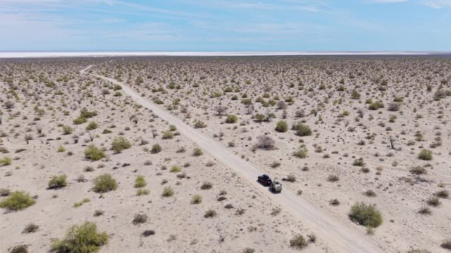 An SUV with a teardrop camper trailer drives through the dry desert in Baja California near the El Salar salt flats.