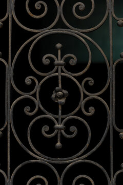 Ornamental wrought iron pattern with vintage scrollwork design, decorative metal gate detail with symmetrical curves on dark background