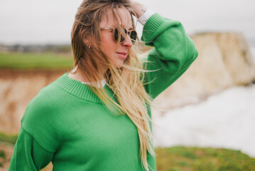 Woman in green sweater stands near cliffs © Reuben