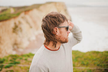 Man with tousled hair and glasses stands at cliffside © Reuben