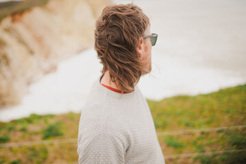Man stands by cliff, gazing at crashing waves © Reuben