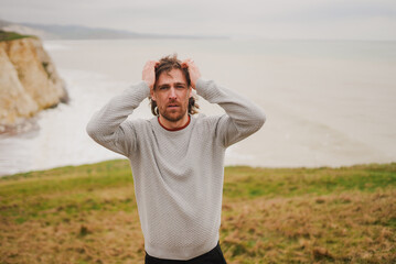 Man stands on grassy cliff, hands on head © Reuben