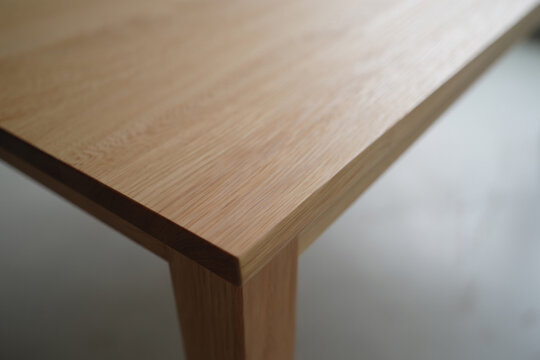 Clean wooden table top corner with blurred background, furniture detail with natural wood grain texture showing, modern interior design element and surface
