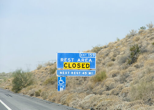 Rest area sign on the 10 freeway with closed sign over it. Desert landscape along the side of the road