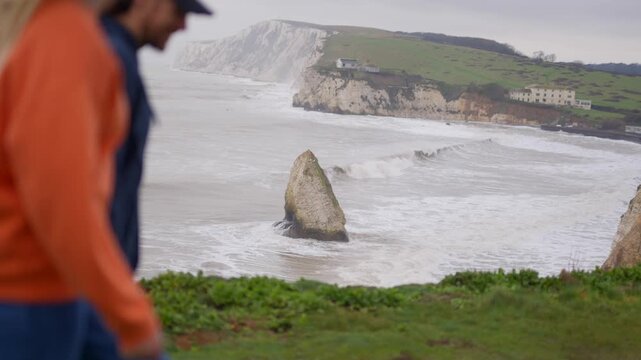 Woman points towards dramatic sea stack on a coastal cliffside landscape