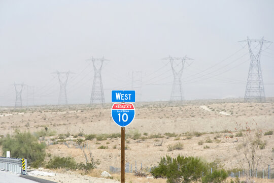 West highway 10 sign on the side of the interstate, row of tall power lines in the background, desert landscape of Southern California.