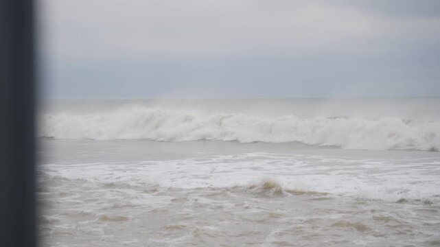 Choppy ocean waves crash against a grey beach under overcast skies