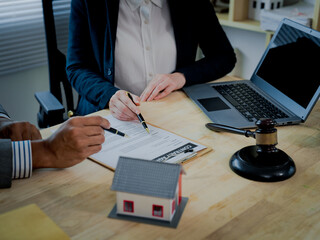 A close-up image of businessmen and lawyers, depicting concepts related to real estate law and auctions: a judge's gavel, a house model, and legal documents on a wooden table. © ArLawKa