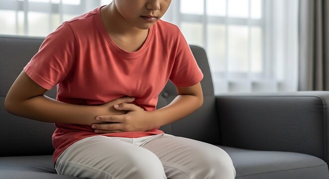A young person on a couch holds their abdomen, displaying discomfort and pain
