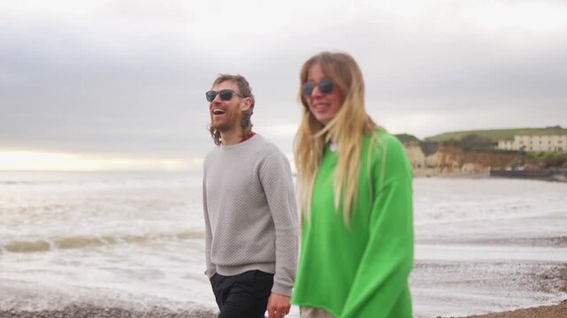 Couple strolls along a sandy beach holding hands on a cloudy day