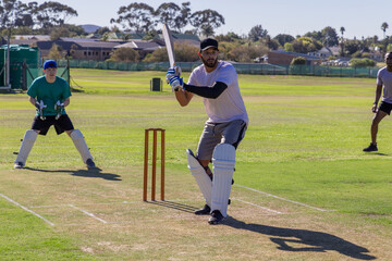 Obraz premium Diverse teammates batting and fielding on suburban cricket pitch, bats, pads, nets visible