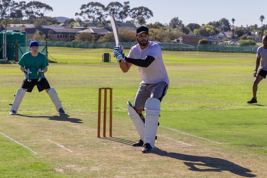 Diverse teammates batting and fielding on suburban cricket pitch, bats, pads, nets visible