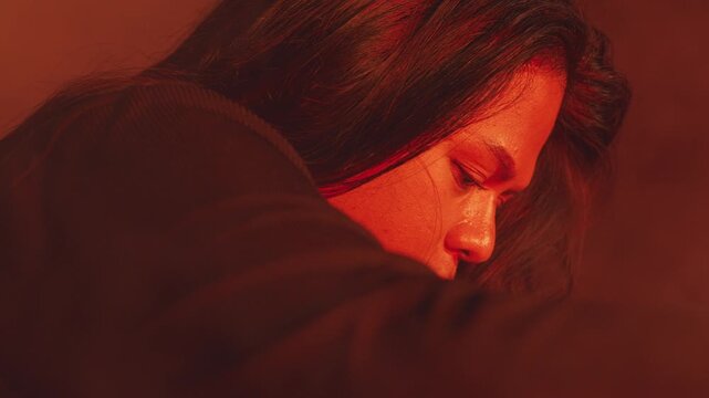 A moody side profile of a woman with her head bowed, resting in deep scarlet illumination. The composition suggests profound sadness, quiet reflection, or the heavy burden of depression.