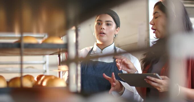 Vertical video: Chef in coat talking at rack of rolls in bakery, peer tapping tablet, noting goods