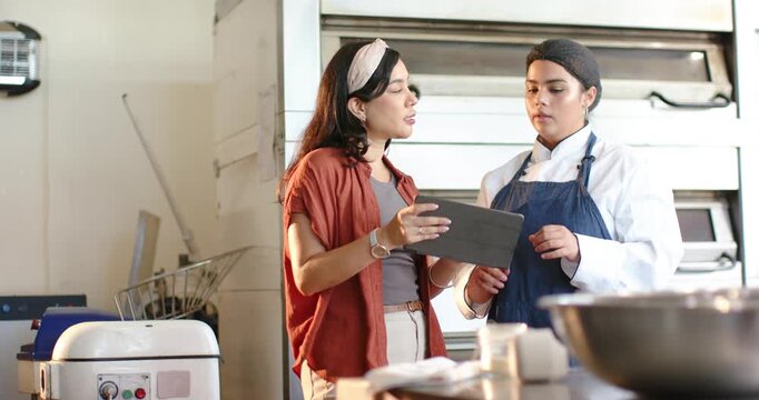 Female Hispanic manager holding tablet, pointing, African American chef in coat reviewing tasks