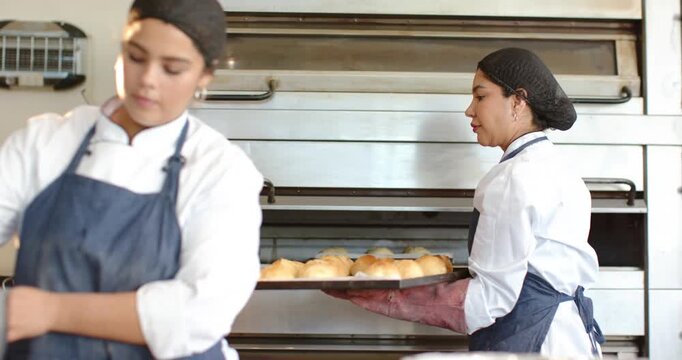 Diverse female bakers responding to oven timer, carrying metal trays to rack while preparing glaze