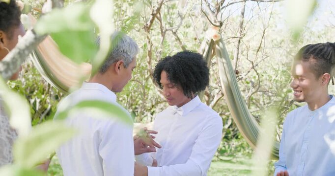 Sliding wedding ring from box, pair wearing white shirts and bowtie in orchard with draped fabric