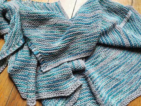 Handmade knitted shawl with striped pattern laid on wooden floor
