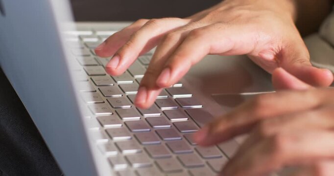 Typing adult male hands moving across laptop keyboard on lap in room, short sleeves, silver laptop