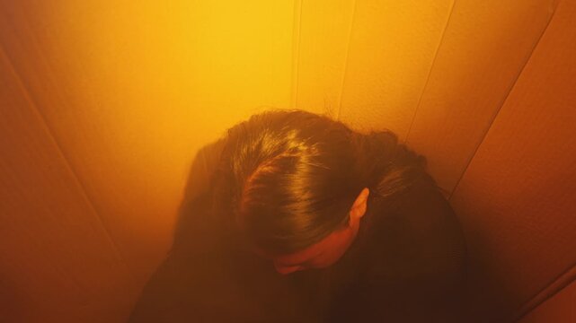 A deeply sad individual sits slumped in a tight, box-like space under yellowish lighting. Highlights themes of being trapped, severe depression, isolation, or overwhelming life pressure.