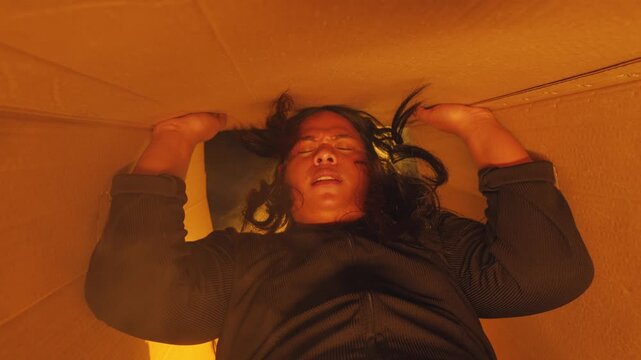 Looking up from inside a box as a woman's face peers down, sealing the flaps closed. Warm atmospheric light fills the space, depicting concepts of abandonment, moving, or storage.
