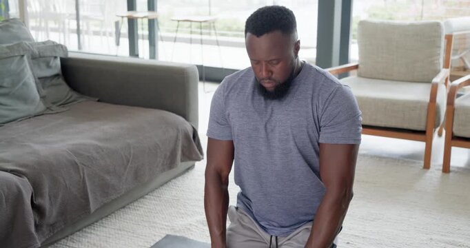 Adult African American man in tee settling on yoga mat at home, starting breathwork, calming mind
