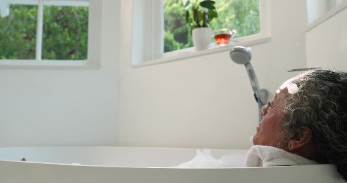 African American senior woman reclining in tub, after foam shaping and blowing to relax, copy space