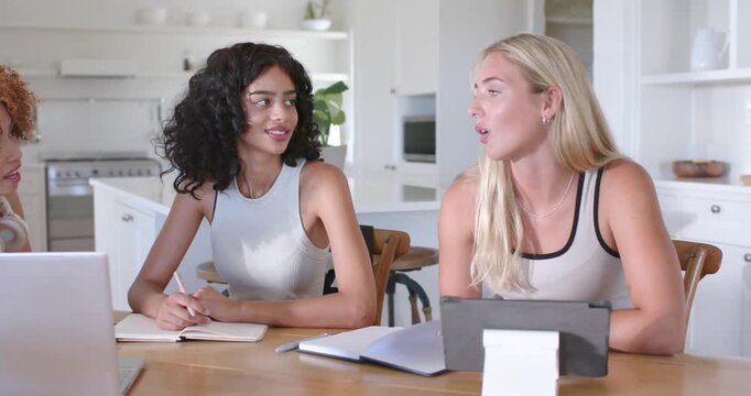 Diverse women collaborating at table in kitchen right woman proposing center woman writing in notes