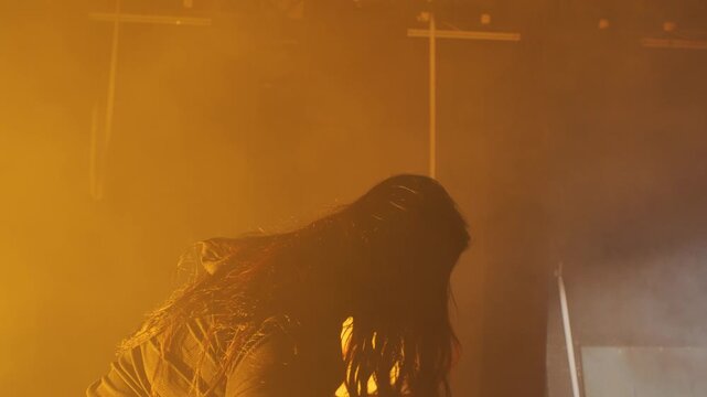 A distressed young woman on a smoky, dramatically lit stage is surrounded by actors holding signs with abusive text, representing verbal abuse, bullying, and societal judgment.