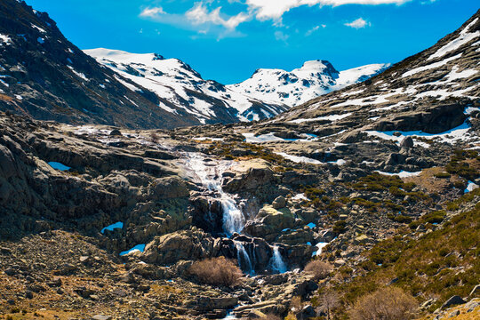 Hermosa cascada de monta&ntilde;a fluyendo por terreno rocoso con picos nevados.