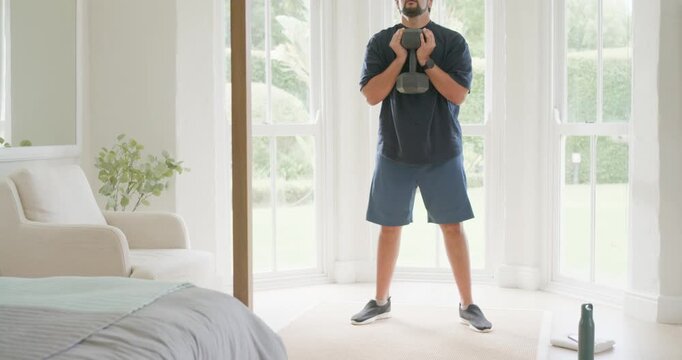 Mid-adult African American man starting kettlebell goblet squats, then checking abdomen in bedroom