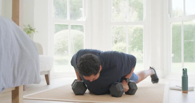 Starting plank using hex grips mid30s African American man doing pushups by windows drinking bottle